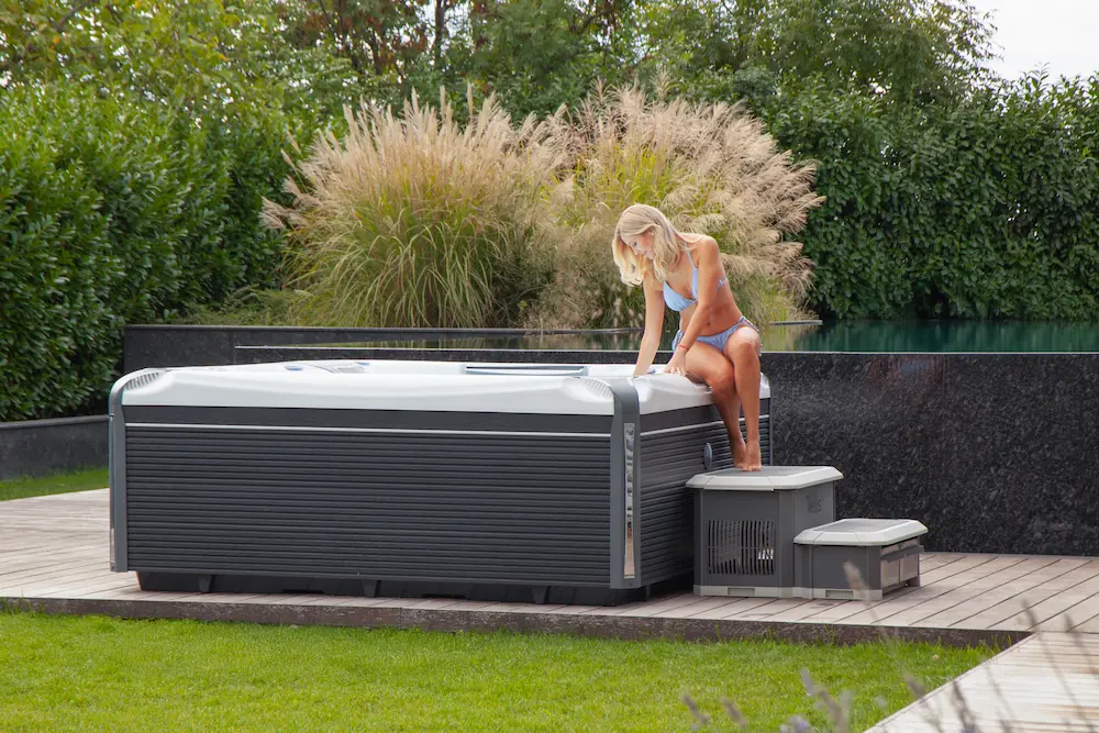 Spa Wellis exterior con cubierta térmica en deck de madera junto a jardín de gramíneas